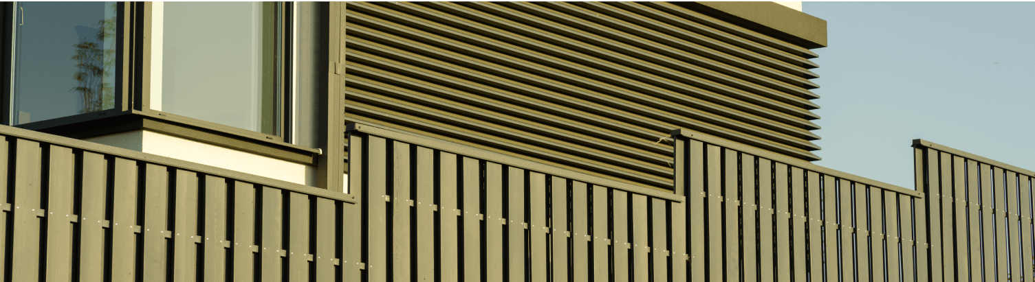 Fassade eines modernen Gebäudes mit WPC-Paneelen und horizontalen Metalllamellen im Sonnenlicht.