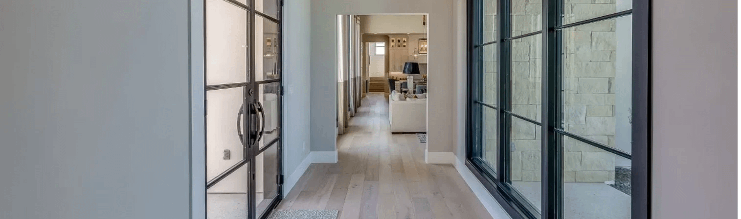 Flur mit hellem Bodenbelag, Glastüren und großen Fenstern, die zum Wohnzimmer führen.