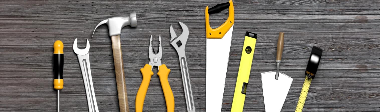 Handwerkzeuge wie Hammer, Säge und Schraubenschlüssel, die auf einem Holzfußboden ruhen.