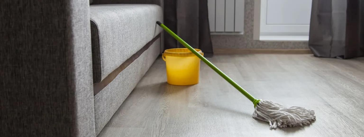 Ein gelber Eimer und ein Mopp auf einem aufgeräumten Holzboden, bereit für die Reinigung von Vinylböden.