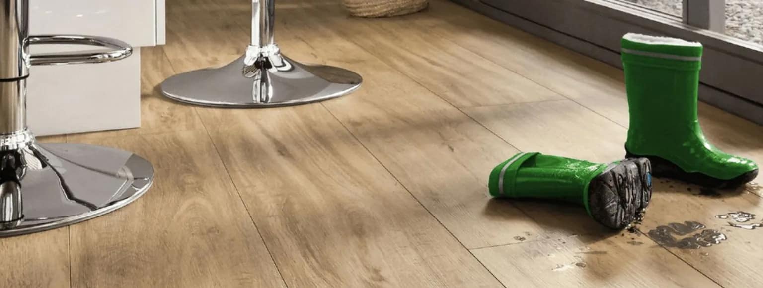 Grüne Regenstiefel auf Vinylboden mit schlammigen Fußspuren neben silbernen Metallbarhockern.