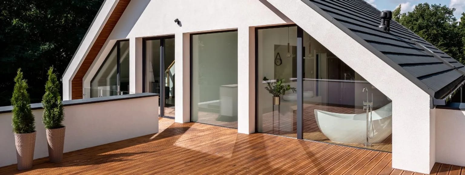 Dachterrasse mit Holzbrettern, großen Glasfenstern und grünen Topfpflanzen.