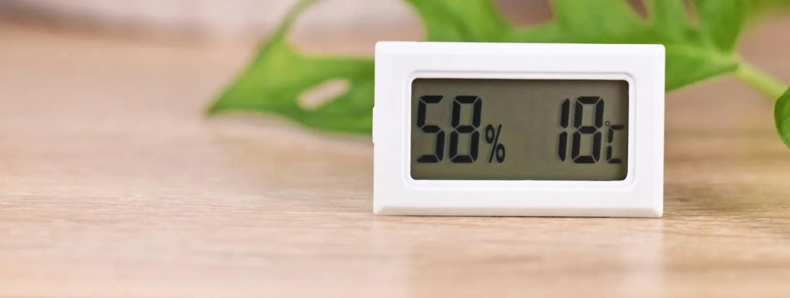 Digitales Hygrometer misst Luftfeuchtigkeit und Temperatur auf einem hellen Holzboden.