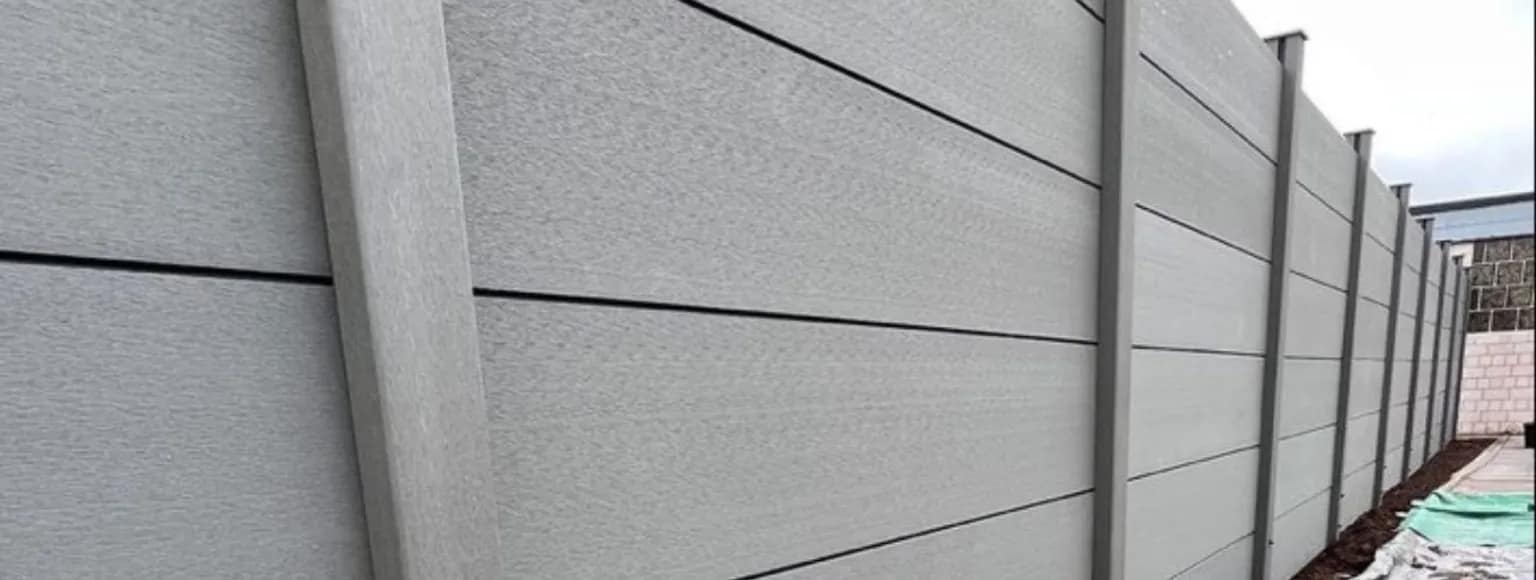 Ein grauer Verbundstoffzaun mit horizontalen Paneelen sorgt für Privatsphäre in einem Gartenbereich.