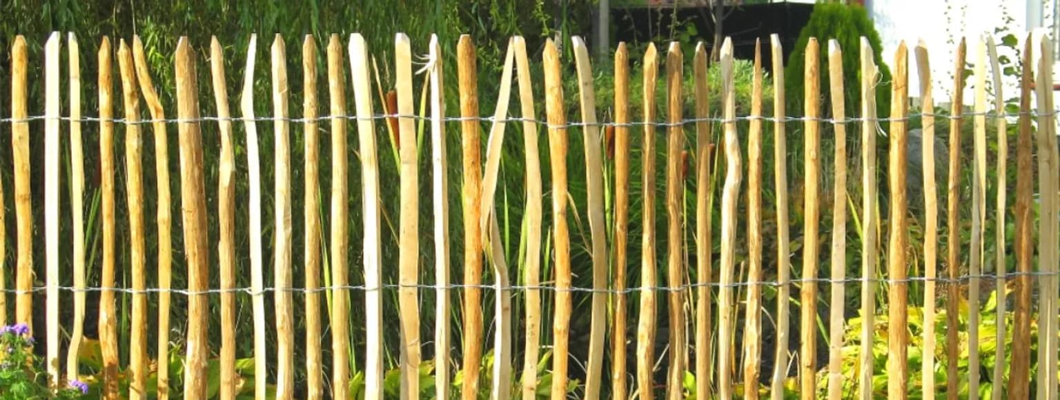 Ein hölzerner Staketenzaun, umgeben von Grünpflanzen in einer Gartenanlage.