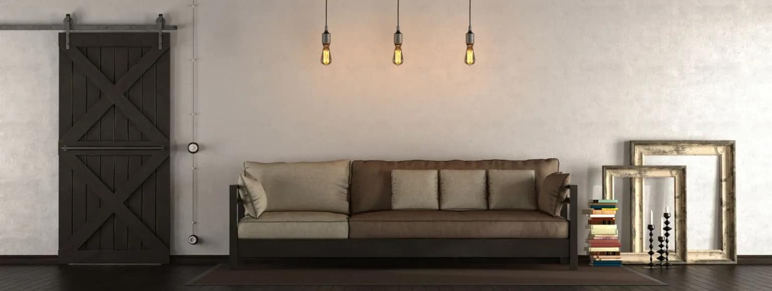 Ein modernes Wohnzimmer mit grauem Sofa, Pendelleuchten, einem Scheunentor und Bücherregalen.