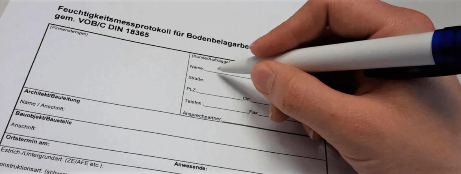 Eine Person schreibt mit einem blauen Stift auf einem Tisch in ein Formular zur Messung der Feuchtigkeit von Fußböden.