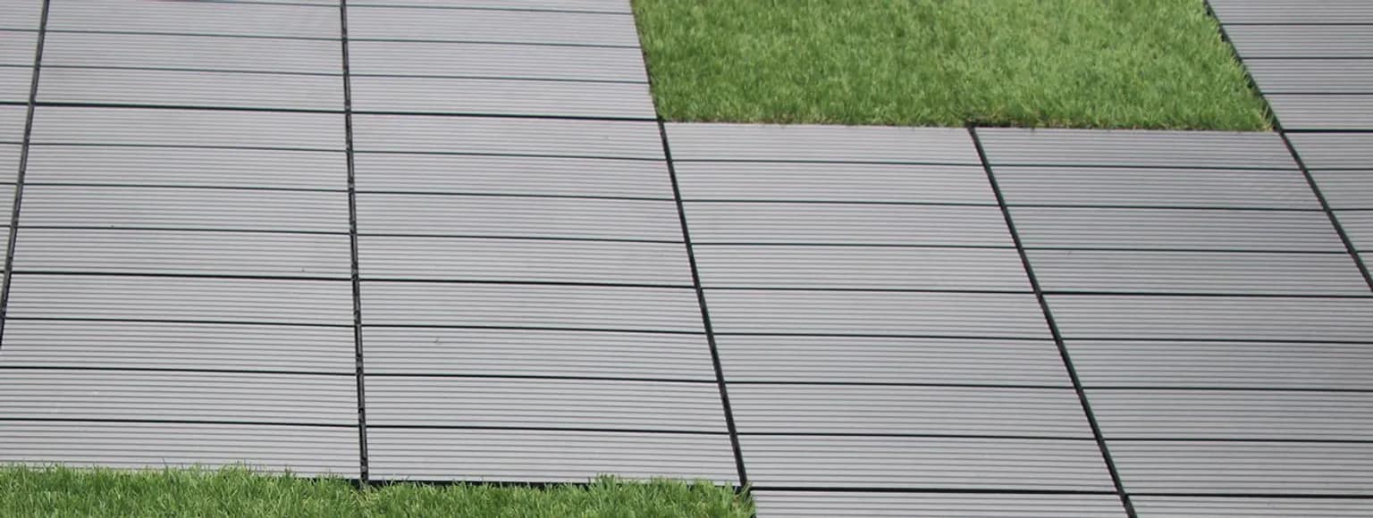 Graue Klickfliesen im Außenbereich mit grünen Grasstreifen zwischen den einzelnen Reihen, Tageslichtszene.