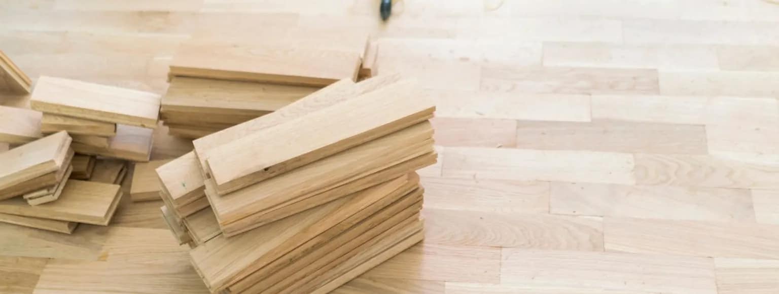 Mehrere Stapel von Fertigparkett-Dielen auf einem teilweise verlegten hellen Holzboden.